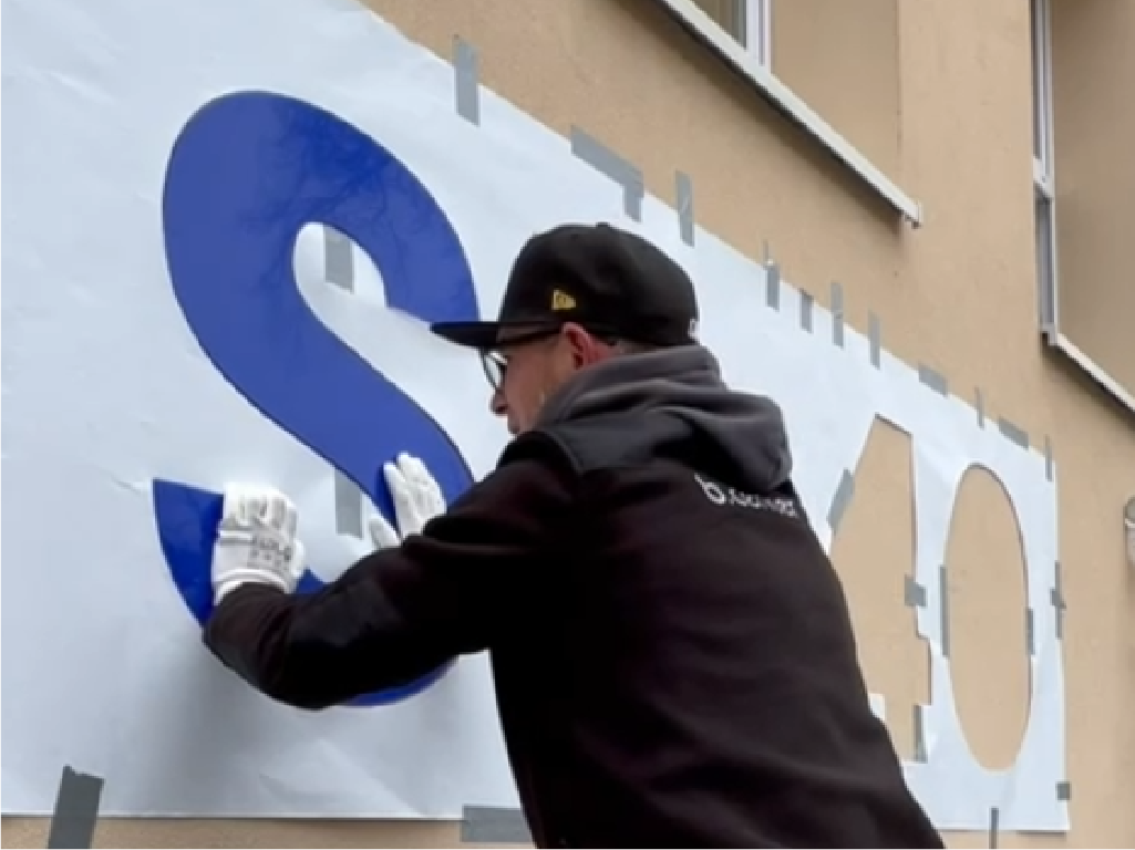 Aplikacja liter przestrzennych 3D. Montaż dużych liter SP 40 na tablicy reklamowej przez pracownika.