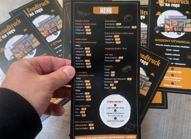 Czarne ulotki reklamowe z menu gastronomicznym. Ulotka trzymana w ręce.