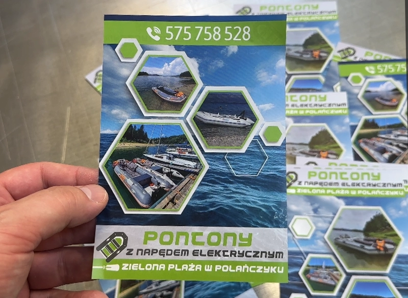 Ulotka reklamowa trzymana w ręce, przedstawiająca pontony na wodzie. Ulotki wynajem sprzętu wodnego.