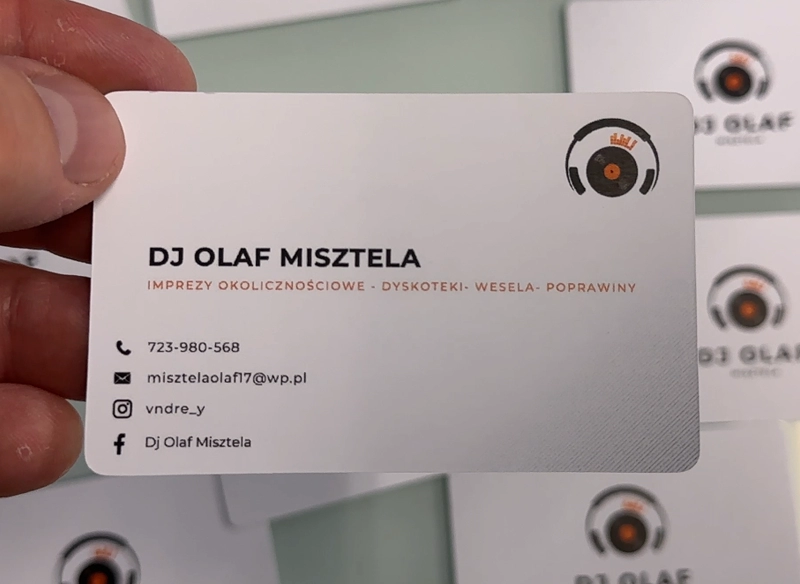 Wizytówka reklamowa trzymana w ręce, biała z grafiką słuchawek i płyty winylowej.