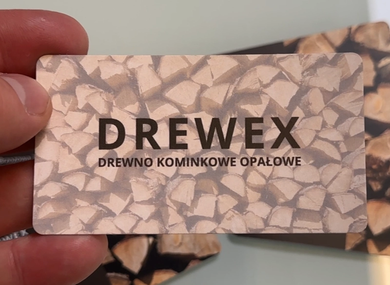 Wizytówka reklamowa trzymana w ręce, z grafiką drewna opałowego. Wizytówka z logo.