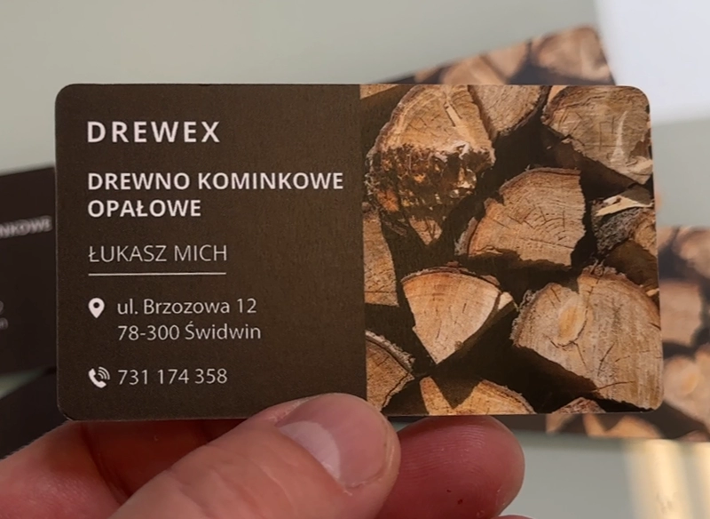 Wizytówka reklamowa trzymana w ręce, z grafiką drewna kominkowego. Wizytówka dostawa drewna.