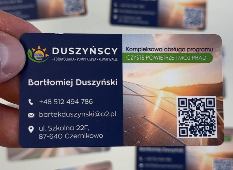 Wizytówka reklamowa trzymana w ręce, niebieska z grafiką paneli słonecznych.