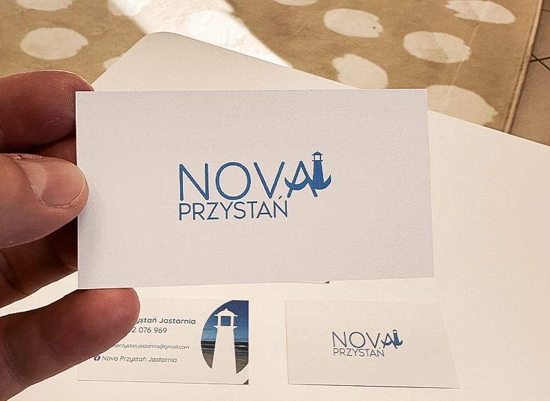 Wizytówka reklamowa trzymana w ręce, biało-niebieska z logo latarni morskiej.