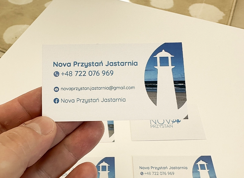Wizytówka reklamowa trzymana w ręce, biało-niebieska z latarnią morską. Wizytówki z logo.