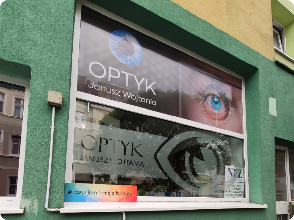 Oklejanie witryny optyka folią One Way Vision. Efektowna reklama na szybach, grafika oka na oknie wystawowym.