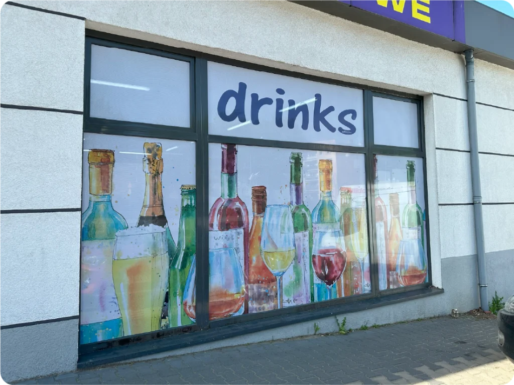 Oklejanie witryny sklepu z napojami folią OWV. Grafika reklamowa na szybach, efektowne oklejanie okien.