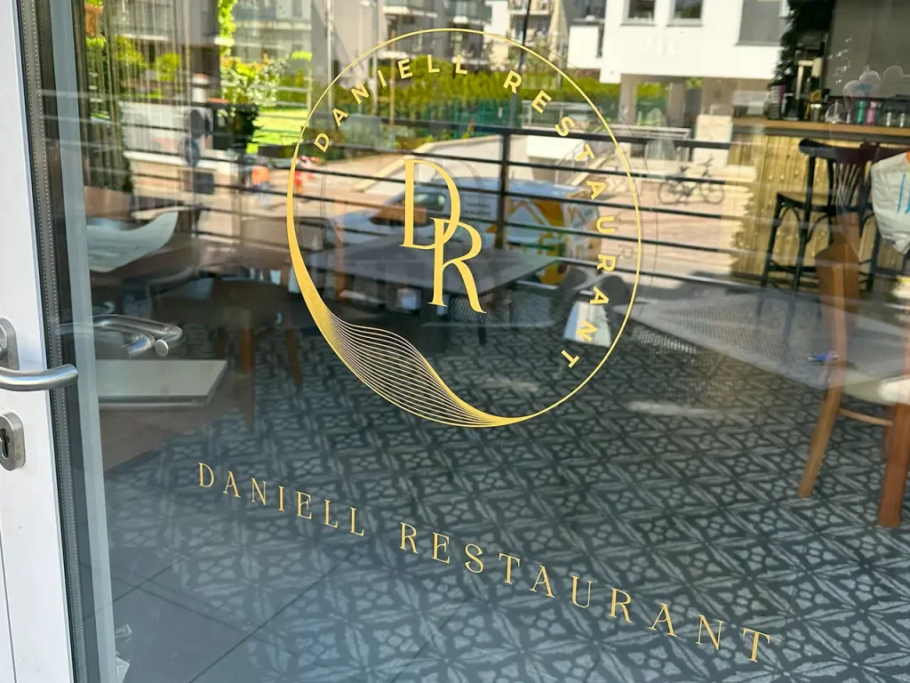 Oklejanie witryny restauracji złotą folią. Reklama na szybach, grafika na oknach ploterową folią.
